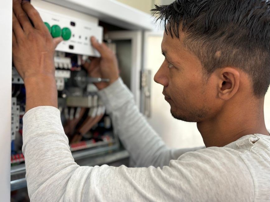 Electrician commissioning a panel with a torch during maintenance work